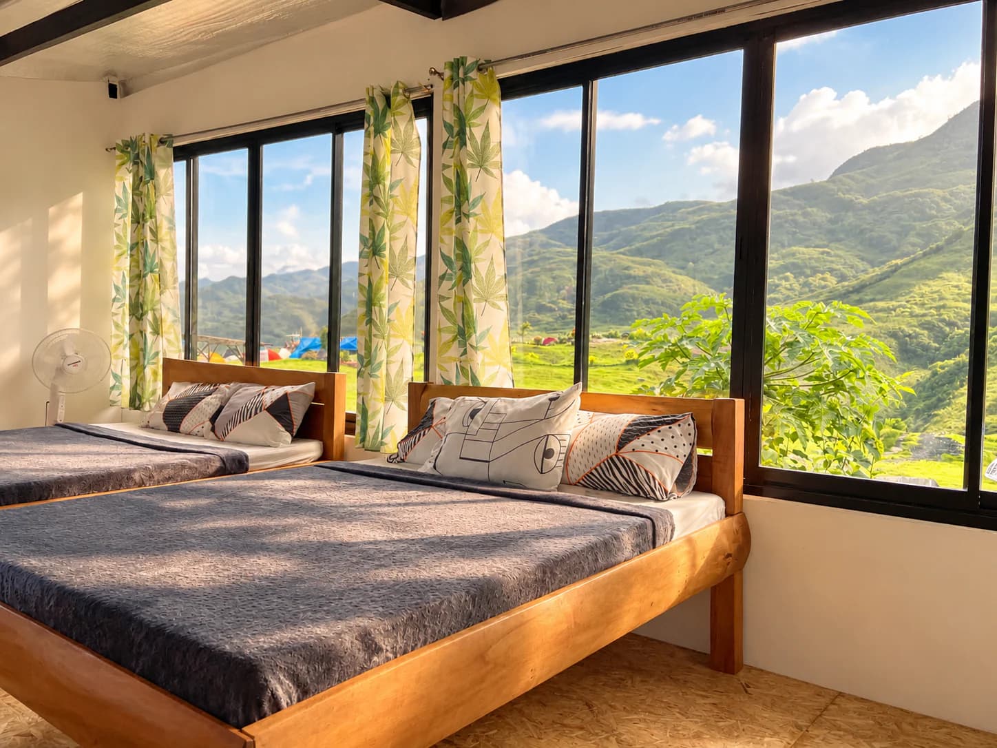 A bedroom in Barkadahan Cottage Tres with two beds beneath tall windows framing the mountains
