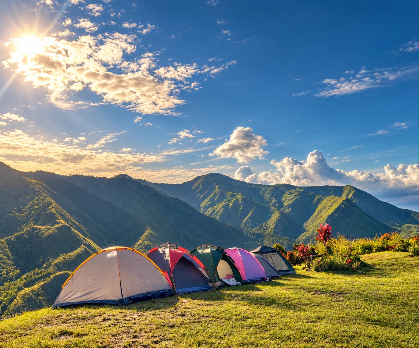 A row of dome tents pitched on the grass ridge, with green mountains and a bright blue sky beyond